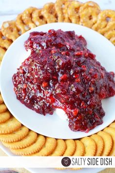 a white plate topped with crackers covered in cranberry sauce next to pretzels