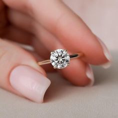 a woman's hand holding an engagement ring with a diamond in the middle, on top of her finger