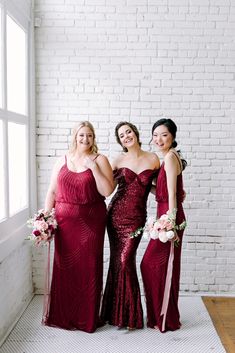 three bridesmaids pose for a photo in front of a brick wall and window