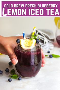 a person holding a glass filled with blueberry lemonade