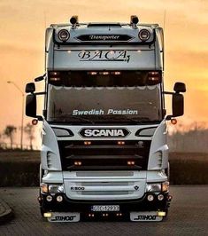 the front end of a white truck parked on a brick road at sunset with its lights on