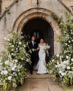 a bride and groom walking out of an archway with flowers in the foreground on their wedding day