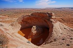 a large hole in the side of a mountain filled with sand and water surrounded by desert terrain