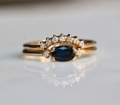 two gold rings with an oval blue sapphire and diamond set on each ring, sitting on a white surface