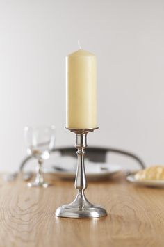 a lit candle sitting on top of a wooden table next to a plate with bread