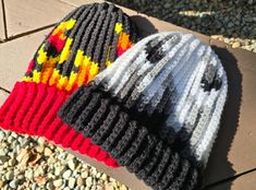 two knitted hats sitting on top of a wooden bench next to gravel and rocks