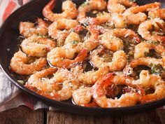 a skillet filled with cooked shrimp and parmesan cheese on a wooden table