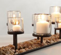 three lit candles sitting on top of rocks in front of a mirror with pebbles around it