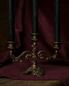 two black candles on a table with a red cloth in the background and gold trimmings