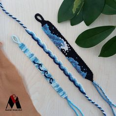 three blue and white beaded bracelets on top of a wooden table next to green leaves