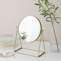 a mirror sitting on top of a table next to a vase with a plant in it