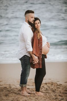 a pregnant woman standing next to a man on the beach with her belly wrapped up