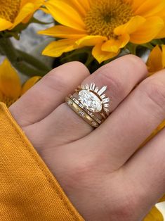 a person's hand with two rings on it and yellow flowers in the background