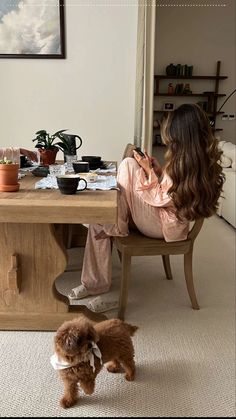 a woman sitting at a table with her dog looking at the food on the table