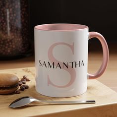 a pink and white coffee mug sitting on top of a wooden table next to a spoon