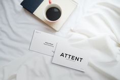 a cup of coffee sitting on top of a bed next to an envelope with the word attent