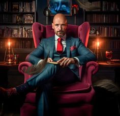 a man sitting in a red chair with his feet up on a book and wearing a suit