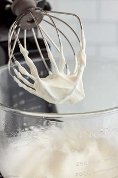 a whisk in a glass bowl filled with whipped cream on top of a mixer