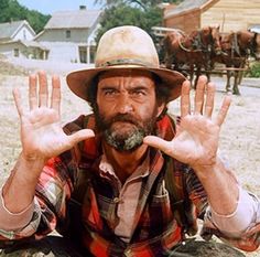 a man sitting on the ground with his hands up in front of him and two horses behind him