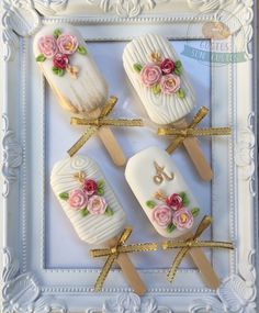 three pops decorated with flowers and ribbons on top of a white plate in a frame