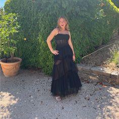 a woman standing in front of a bush wearing a black dress