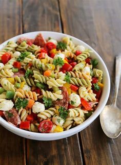 a white bowl filled with pasta salad on top of a wooden table next to a spoon