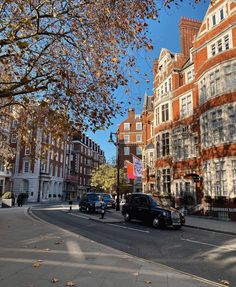 cars are driving down the street in front of tall buildings and trees with leaves on them