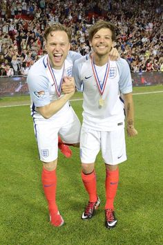 two soccer players are standing on the field with their arms around each other and holding medals