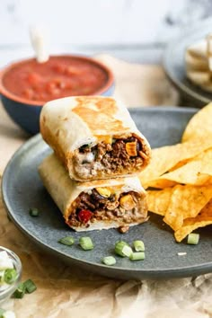 a burrito cut in half on a plate next to chips and salsa sauces