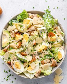 a salad with hard boiled eggs and parmesan cheese in a bowl on a white surface