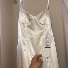 a white dress hanging on a hanger next to a person's hand holding a tag