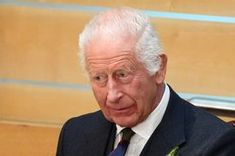 an older man wearing a suit and tie sitting in front of a wooden table with flowers on it