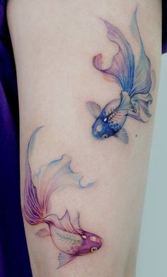 a woman's leg with two goldfish tattoos on it, one is blue and the other is pink