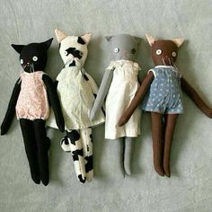 five stuffed cats are lined up on the floor in front of each other, one is wearing a dress