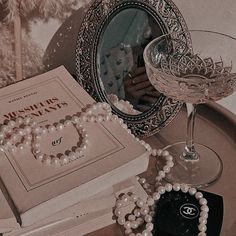 a table topped with a book and a glass filled with pearls next to a mirror