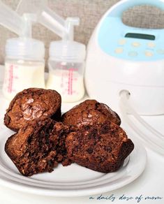 three chocolate muffins on a white plate next to a baby bottle