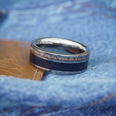 two wedding bands sitting on top of a pair of blue jean jeans with a leather wallet in the background