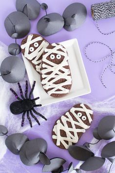 halloween cookies decorated with white icing and black spider decorations on a purple tablecloth