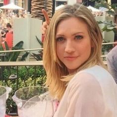 a woman is sitting at a table with wine glasses in front of her and pointing to the camera