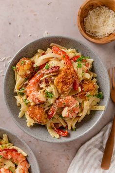 two bowls filled with pasta and shrimp on top of a white table next to silverware