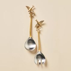 two spoons with birds on them sitting next to each other in front of a beige background