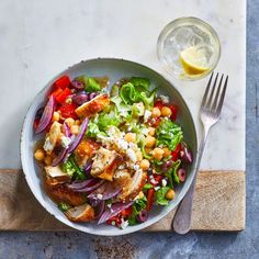 a salad with chicken, lettuce and chickpeas in a bowl next to a glass of water