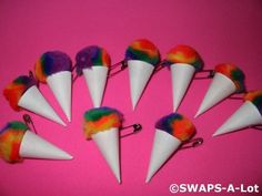 six white cones with multi - colored pom poms on each one are lined up against a pink background