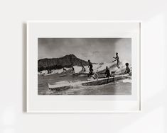 a black and white photo of people on surfboards in the water with mountains in the background