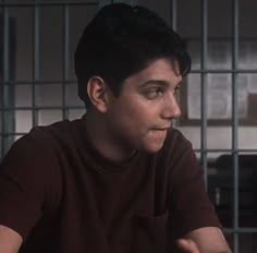 a young man sitting in front of a jail cell with his hand on his hip