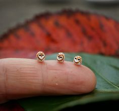 two small gold studs sitting on top of a leaf next to a person's finger