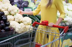 a woman pushing a shopping cart through a produce section in a grocery store with vegetables