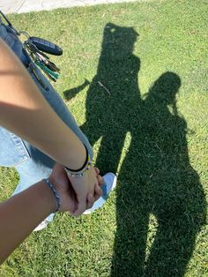 two people holding hands in the grass with their shadow on the ground and one person standing next to them