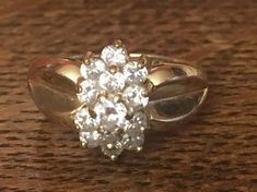 This gorgeous ring features a sparkling cluster of cubic zirconia stones, paired with lustrous 14 karat yellow gold. The band is an approximate size 6.5, and the ring weighs approximately 4.5 grams. This gorgeous piece has a unique tiered cluster of stones at center that adds to its appeal and intrigue. In addition, the shoulders of the band have a unique, heart or leaf shaped detail. This is the ideal piece to buy for yourself, and it would also make a beautiful promise ring, graduation gift, a Cluster Ring With Vs Clarity Cubic Zirconia, Gold Cluster Ring With Vs Clarity, Dazzling Gold Cluster Diamond Ring, 14k Gold Cluster Ring With Prong Setting, Yellow Gold Cluster Ring With Cubic Zirconia, Sparkling Cluster Cubic Zirconia Rings, Sparkling Cluster Jewelry For Anniversary, Diamond Cluster Ring With Vs Clarity, Dazzling Cluster Diamond Ring With Vs Clarity