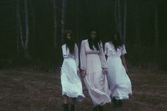 three women in white dresses are walking through the woods with their hands on their hips